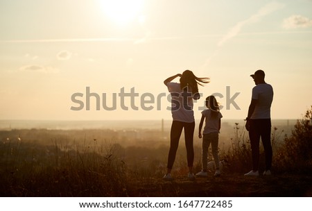 Silhouette of a family standing on the hill with their backs to the camera and looking to the horizon on the sunset, saying goodbye to long and active day
