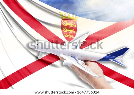 Airplane in hand with national flag of Jersey on a background of blue sky with sunbeams