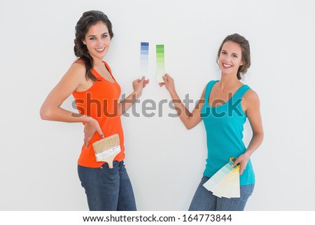 Side view portrait of two female friends choosing color for painting a room against white background