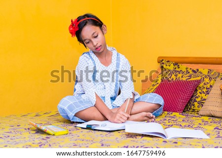 Cute little preschooler child girl studying at home , Indian girl with writing on notebook on bed ,asian girl child reading book