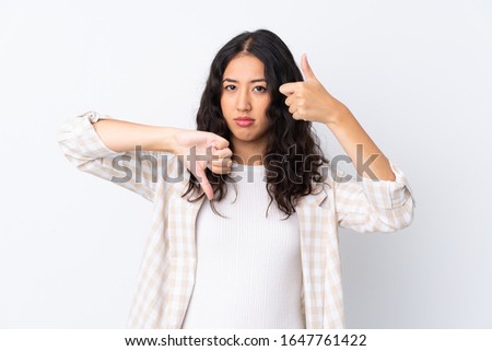 Mixed race woman over isolated white background making good-bad sign. Undecided between yes or not