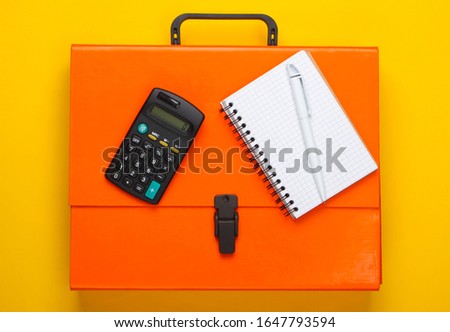 Orange paper case, notebook and calculator on a yellow background. Top view