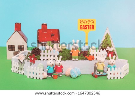 Happy Easter sign and a toy house of bunnies family in the garden and dyed eggs hunt. Greeting card concept.