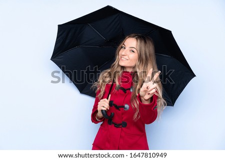 Young woman with winter coat and  holding an umbrella smiling and showing victory sign