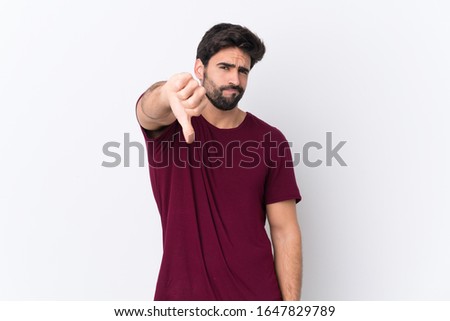 Young handsome man with beard over isolated white background showing thumb down with negative expression