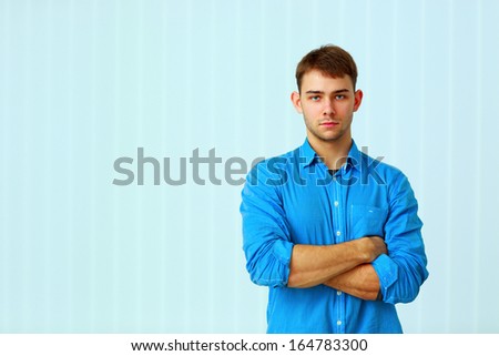 Young pensive businessman standing with arms folded at office
