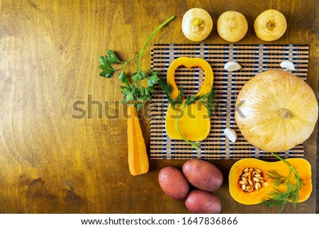 a whole small pumpkin, two pieces of pumpkin, carrots and sprigs of dill and parsley on a cutting bamboo Board, a round pumpkin and turnip on a wooden background, top view, space for text