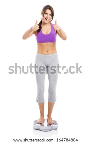 Beautiful athletic woman over a scale with thumbs up, isolated over white background