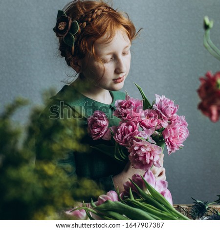A redheaded little girl in a green linen dress fiddles with a bunch of pink tulips.