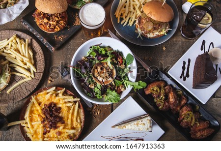 Variety of dishes, classic homemade hamburgers goat cheese salad, french fries and desserts on wooden table. Menu of the restaurant menu.