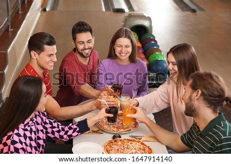 Group of friends with drinks and pizza in bowling club