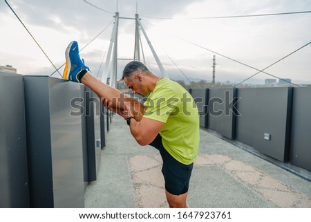 Older well built man in activewear stretching out his legs before running
