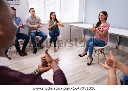 Group Of Young People Learning Deaf Gesture Sign From Woman Sitting On Chair