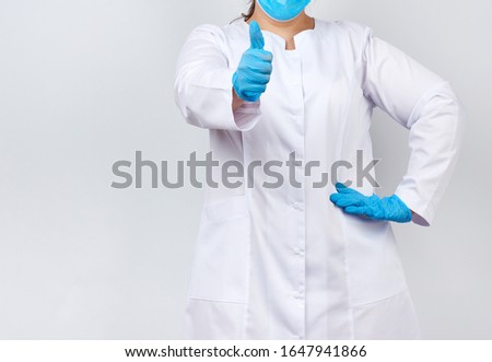 medic woman in white coat and mask, wearing blue medical latex gloves on her hands, showing like gesture in hand, approval concept, copy space