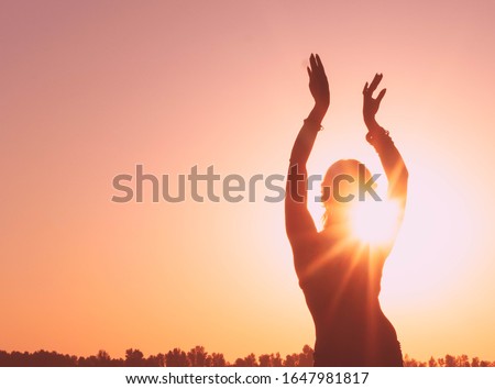 dark glowing silhouette of slim woman with hands up in the air illuminated with sunshine dancing traditional tribal belly dance in front of aurora sky at sunrise Royalty-Free Stock Photo #1647981817