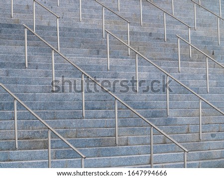 Abstract photo of big stone stairs with metal handrails.