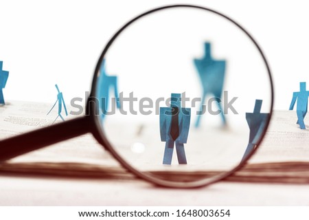 Business recruitment or hiring photo concept. Looking for talent.  Figure of candidates are standing on open newspaper under magnifier.
