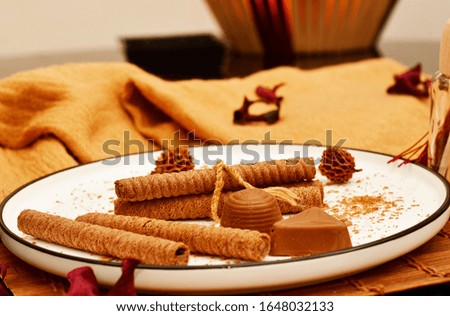 Wafer rolls and chocolate, served in a white round plate with black border.