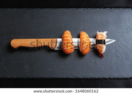 Stock photo of Maki sushi on the edge of a Japanese knife on black graphite background.