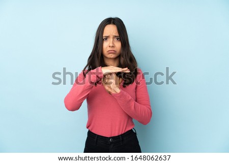 Young mixed race woman isolated on blue background making time out gesture