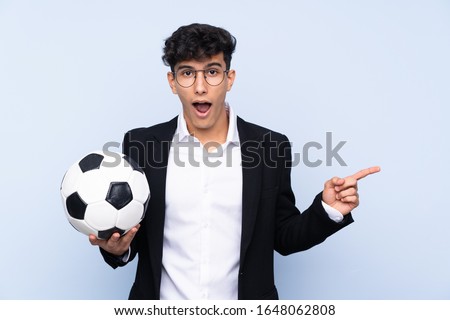 Argentinian Soccer coach over isolated blue background surprised and pointing side