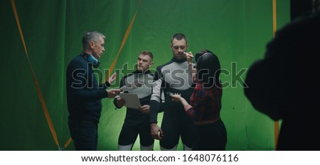 Medium shot of a cosmetician preparing an actor while others discussing over the script before shooting a scene