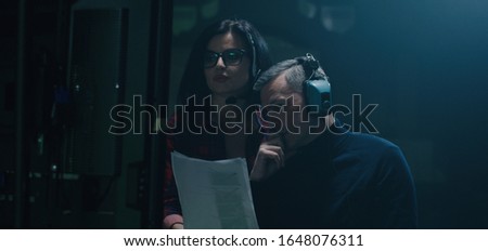 Medium shot of a director holding the script and discussing with a female crew member before a monitor