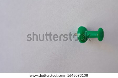 Green pin, attached to a white empty paper, oriented to the right, with copy space
