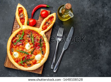 
Easter pizza in the form of a hare with eggs, tomatoes, sunflower oil on a stone background with copy space for your text