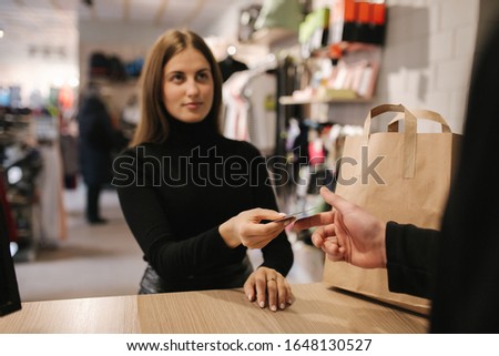 Attractive woman is giving a credit card to shop manager. Customer give credit card to assistant and smiling while doing shopping in boutique