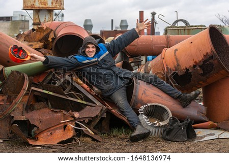 factory roof. work at height. a working man lies on a pile of metal pipes and scrap metal. in a hand a working helmet. jokes in the workplace. neglect of remedies. safety violation Royalty-Free Stock Photo #1648136974
