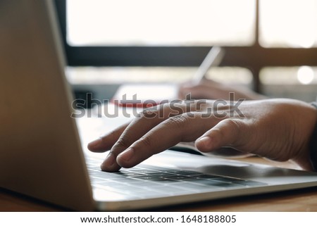 Close up of businessman or accountant hand holding pen working on laptop computer for calculate business data, accountancy document and calculator at office, business concept
