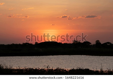 The picture of an orange sunset setting with black mountains and trees.