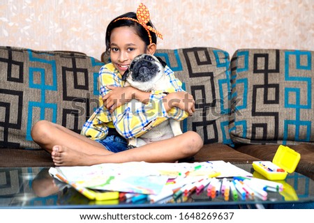 Cute little Indian/ Asian girl playing with her pet dog pug on sofa in her room.