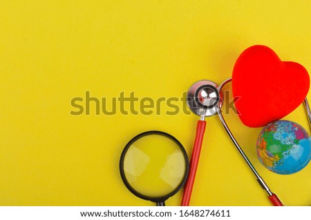 Red heart, stethoscope world globe and magnifying glass on yellow background. Selective focus.
