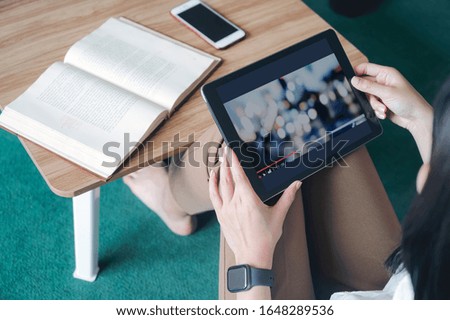 Cropped shot of young woman holding and using tablet while sitting at living room.