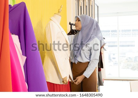 A Muslim woman is checking the quality of dress cloth before sending to customers.. She is very determined and detailed with the creation of the work.  Concept on designing and making product.