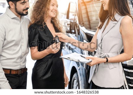 Young couple love receive key with buyers signing contract for new car in auto show. Concept for car rental