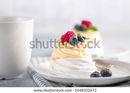 Coffee mug and Pavlova cake with whipped cream and fresh berries on white plate. Scandinavian style. Soft focus - Image