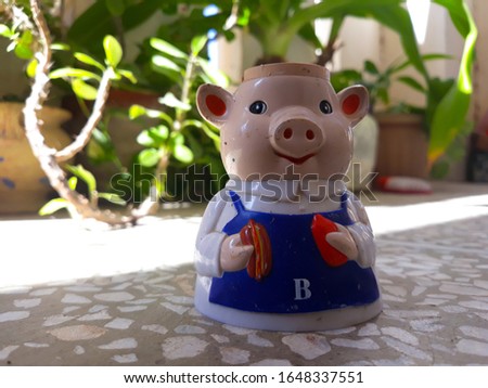 Pig toy in chef getup holding a burger. Closeup of toy. For children. Greenery background.