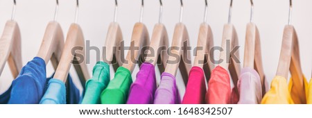 Clothes on clothing rack panoramic banner. Women's wardrobe fashion apparel rainbow organized t-shirts by colors hanging on closet hangers. Shopping spring cleaning. Panorama background.