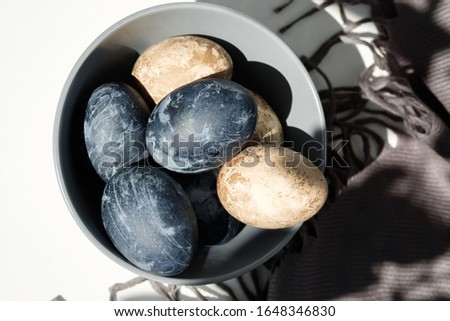 Naturally dyed eggs prepared for Easter on gray texture tablecloth background. Easter background with Easter eggs and feathers in a ceramic gray bowl. 