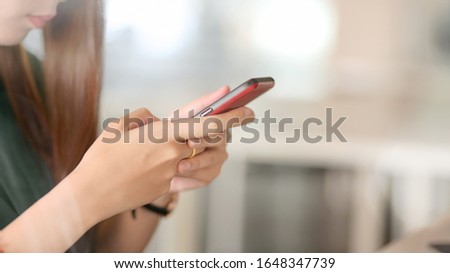 Side view of businesswoman using smartphone while sitting in blurred simple office room background