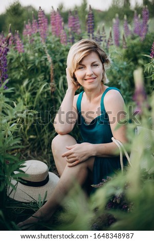 Happy romantic woman in a field of purple lupine flowers looks at the camera and smiles. Soft selective focus. Female portrait.