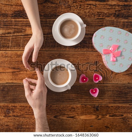 Valentine's Day celebration concept. A nice gift for your loved one. Hands of man and woman with coffee mugs on a wooden table background. Copy space. Flat lay.