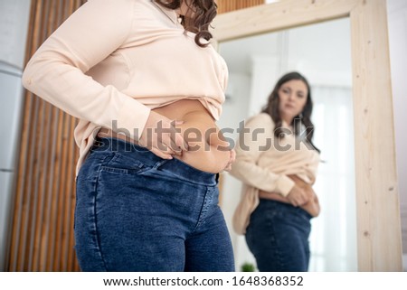 Fat. Young woman in a beige blouse examining her abs Royalty-Free Stock Photo #1648368352