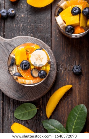 Fresh fruit salad with various kind of berry and citrus fruit, mango served in glass bowl, placed on wooden table. Shot from aerial view, copyspace for text