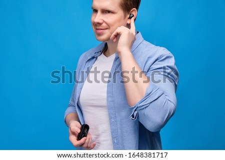 A man in a blue shirt has put on a wireless earpiece and turns on the music. Close up.