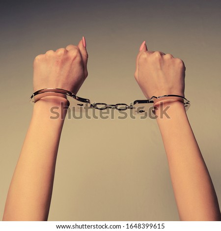 Beautiful female hands with manicure in handcuffs near wall.