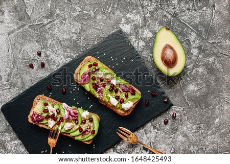 Tasty sandwiches with avocado, goat cheese, italian chicory and pomegranate seeds on wholegrain bread on black feed board. Healthy delicious breakfast or lunch concept. Top view, flat lay, copy space